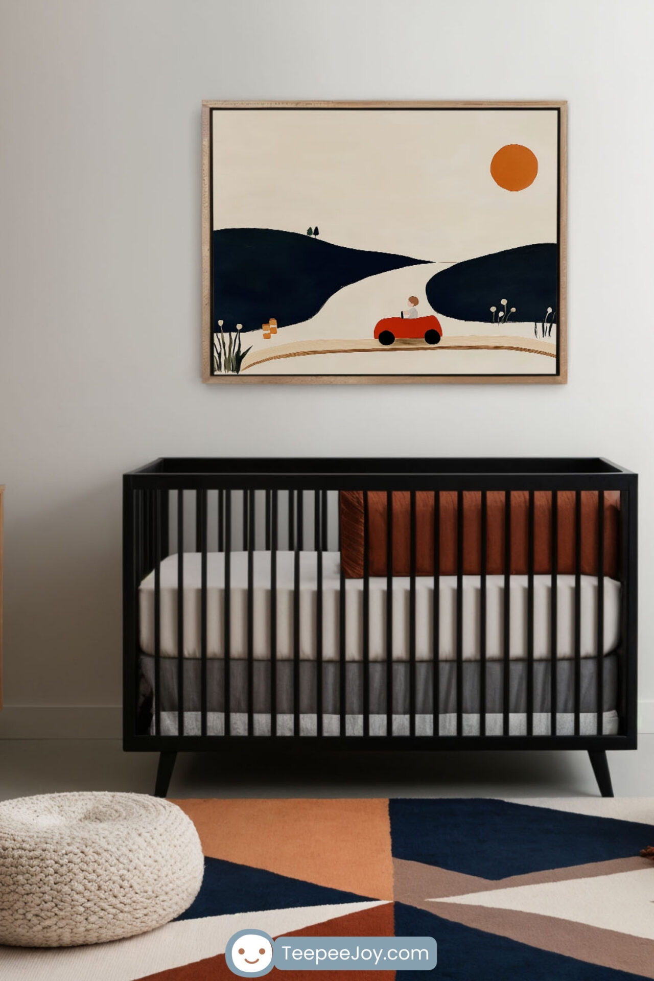 Modern nursery featuring a sleek black crib with a minimalist design, complemented by a white mattress and rust-colored pillows. Above the crib, a framed wall art print showcases a stylized landscape with rolling navy blue hills, a winding road, and a small red car under an orange sun. The room is accented with a geometric-patterned rug in earthy tones and a cozy, knitted pouf, creating a warm and stylish atmosphere.