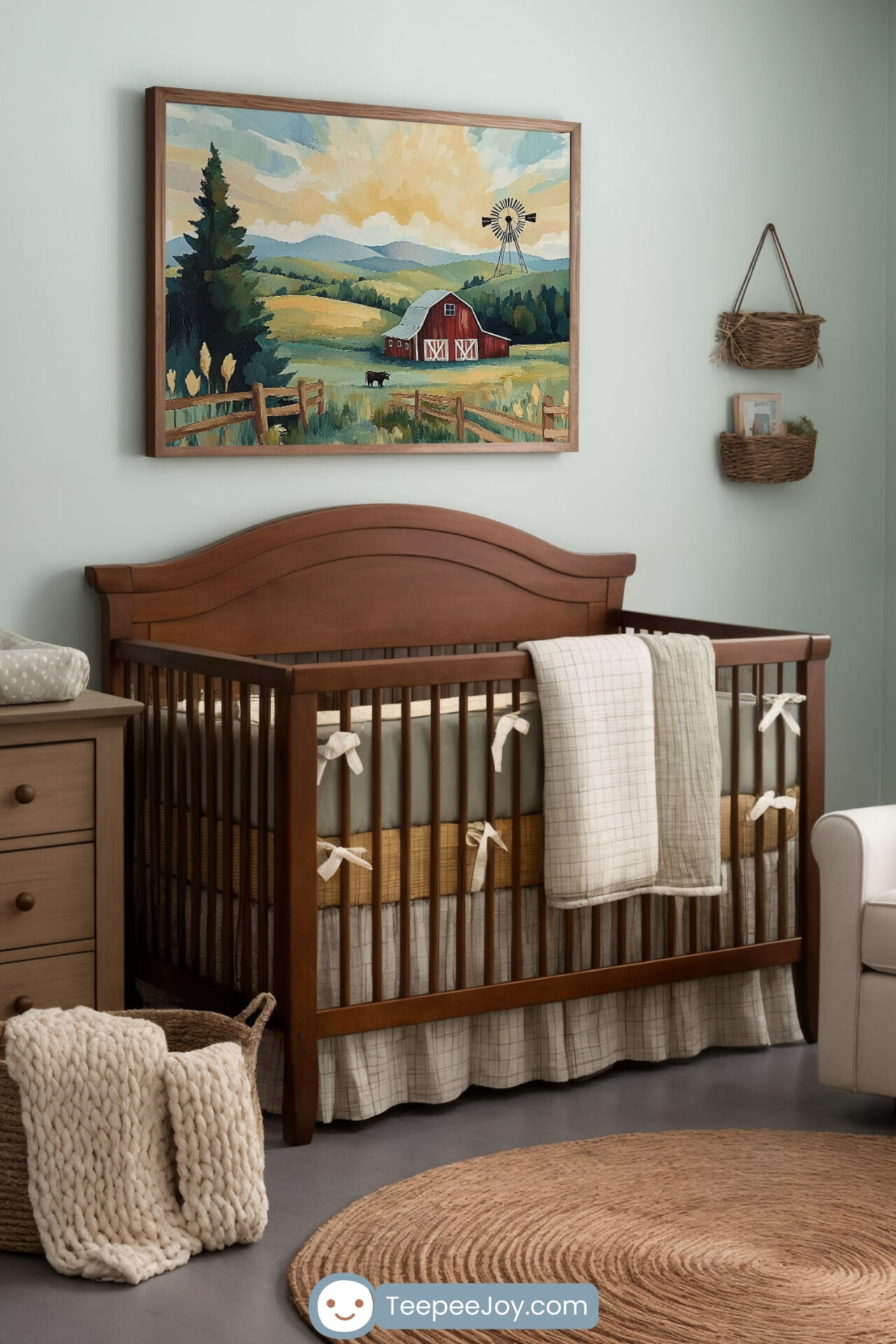 Cozy farmhouse-style nursery with a wooden crib, a beige armchair with a green pillow, and a dresser with a changing pad. A large framed painting of a countryside scene with a red barn, windmill, and rolling hills hangs on the soft green wall. Woven baskets, neutral textiles, and natural wood furniture add to the warm and inviting aesthetic.