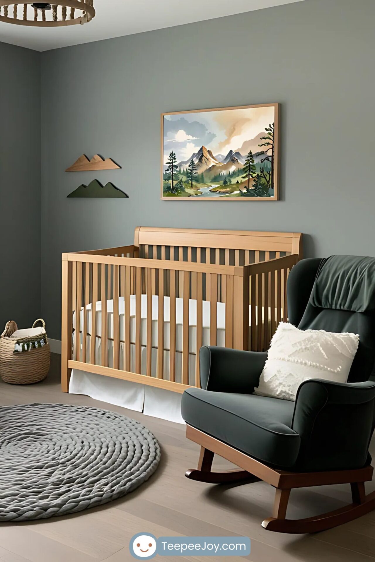 A serene nursery with a wooden crib against a muted green wall, featuring a framed artwork of a mountain landscape with a flowing river and evergreen trees. A dark green rocking chair with a textured white pillow sits nearby, next to a cozy knitted gray rug. Wooden mountain-shaped wall decor and a woven basket add to the rustic, nature-inspired theme.